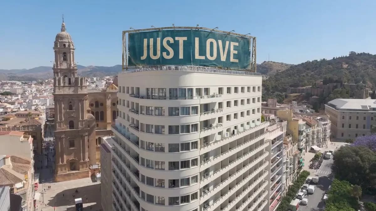 A large sign on the façade of the AC Málaga Palacio hotel reading "JUST LOVE" in bold capitals.