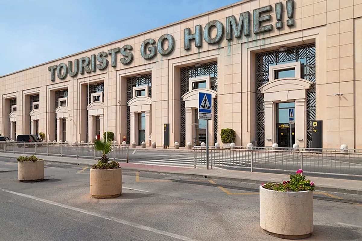 A sign reading "Tourists Go Home!!" in the arrivals area of Málaga airport.