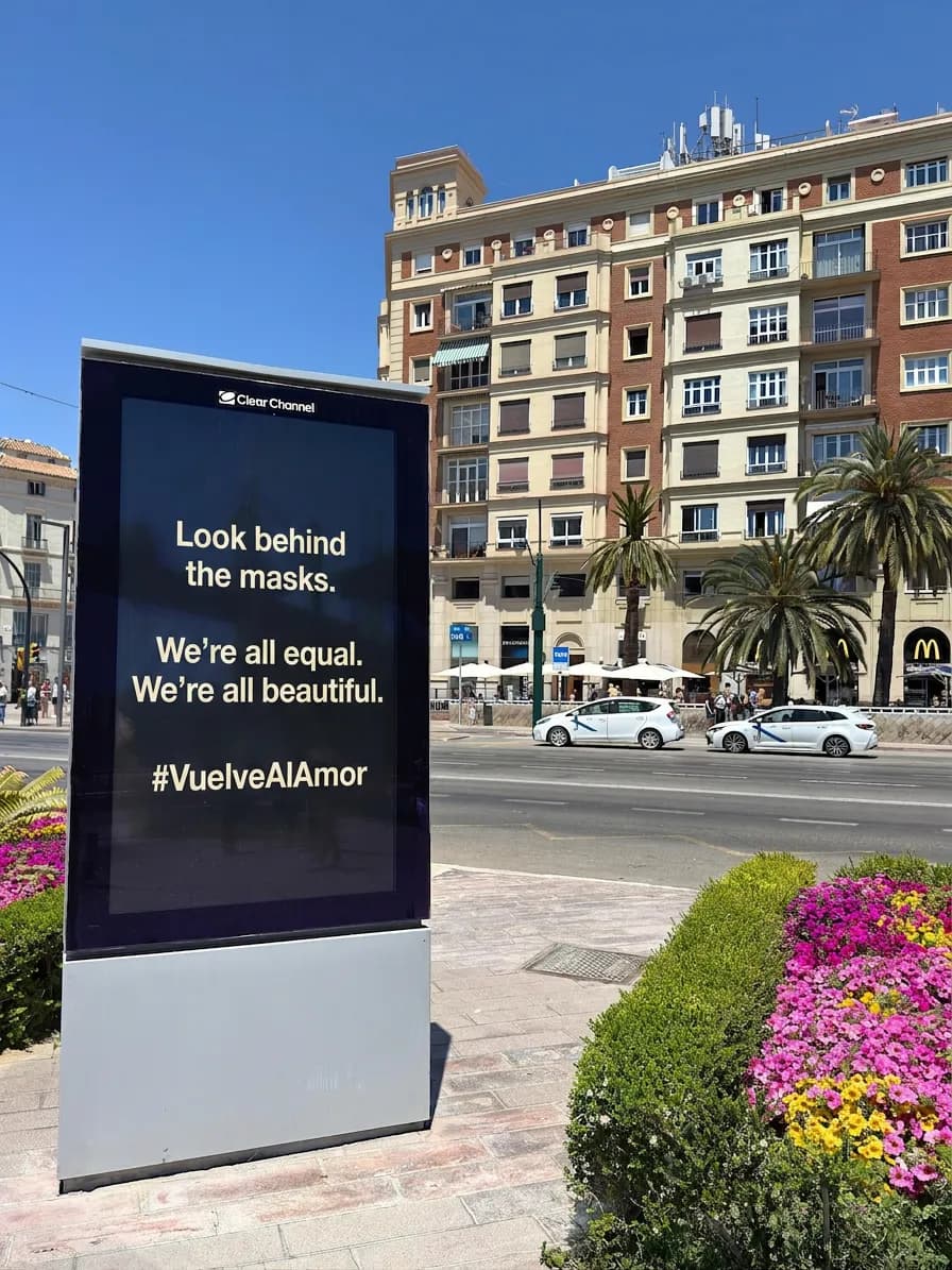 A sign reading "Look behind the masks. We're all equal. We're all beautiful #VuelveAlAmor" near Plaza de la Marina.
