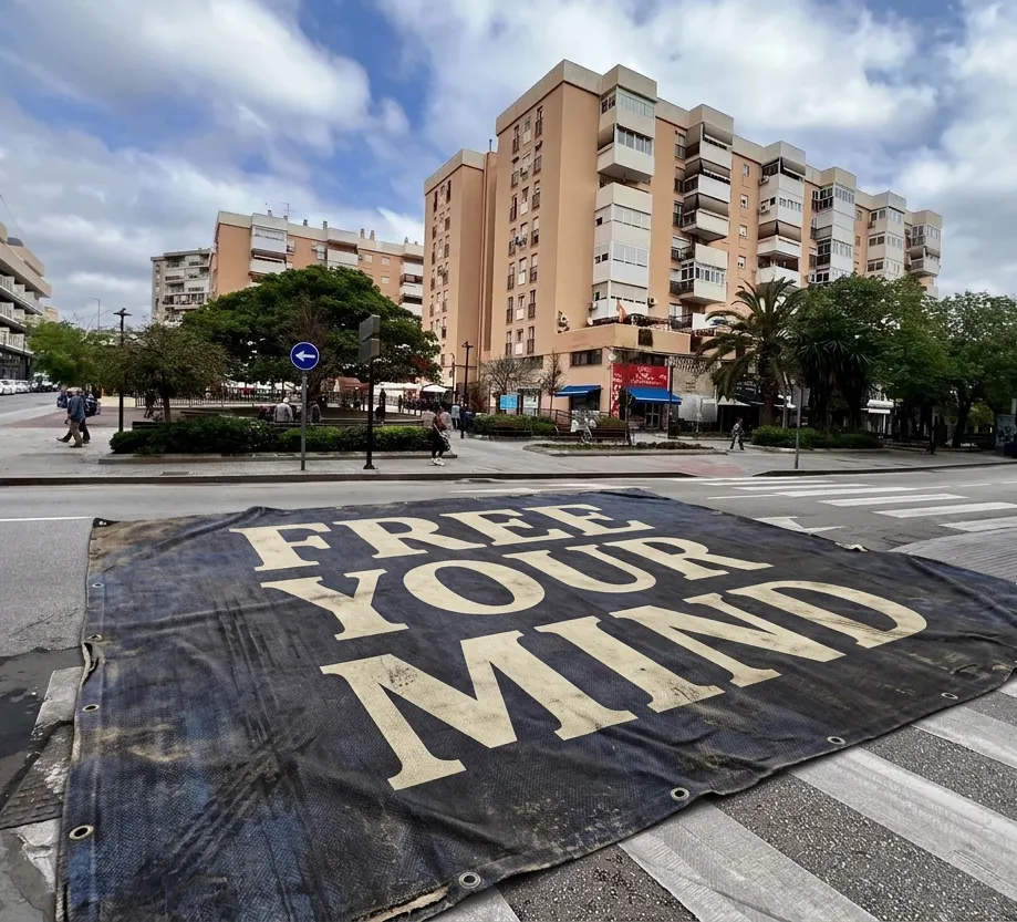 A large banner lying across a street crossing in Málaga, reading "FREE YOUR MIND" in bold capitals.