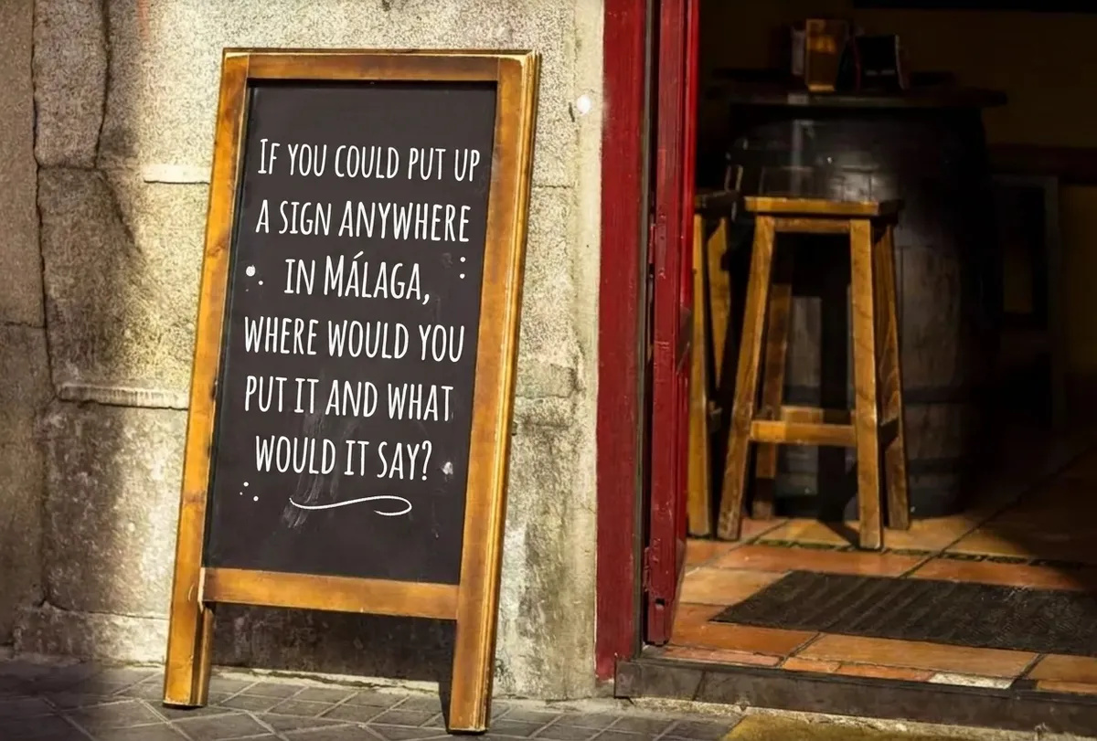 A chalkboard sandwich sign outside a Málaga bar reading "If you could put up a sign anywhere in Málaga, where would you put it and what would it say?"