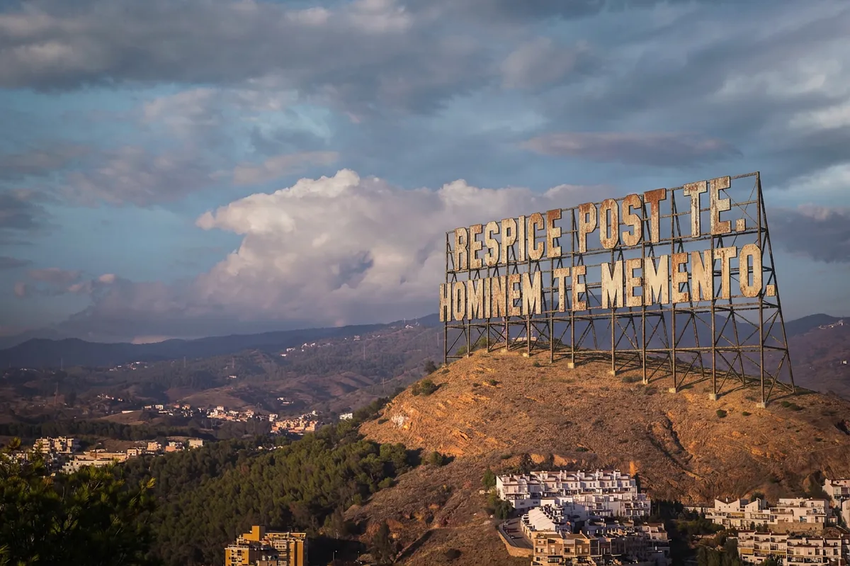 A large sign atop Monte Victoria in Málaga reading "Respice post te. Hominem te memento" in Latin.